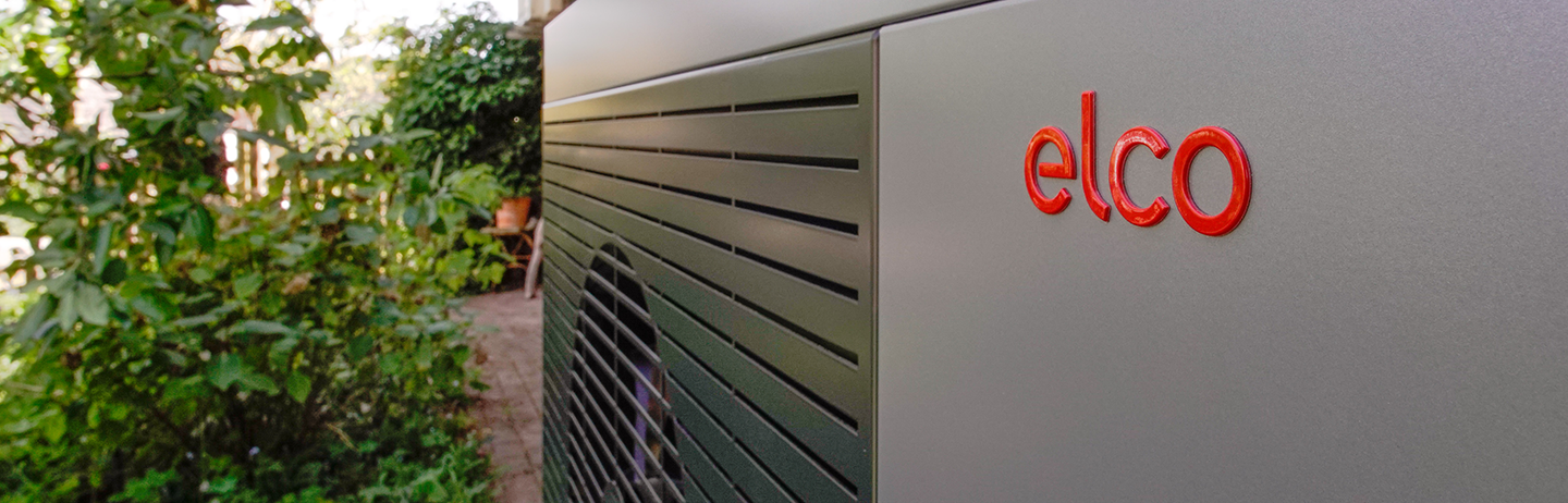 Close-up of a heat pump in a front garden, surrounded by plants