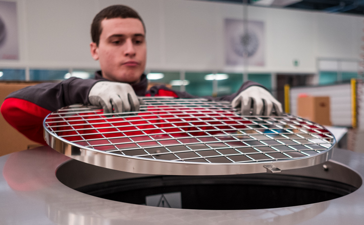 Ein ELCO Mitarbeiter hebt ein rundes Metallgitter an, das den Zugang zu einer großen zylindrischen Maschine abdeckt. 